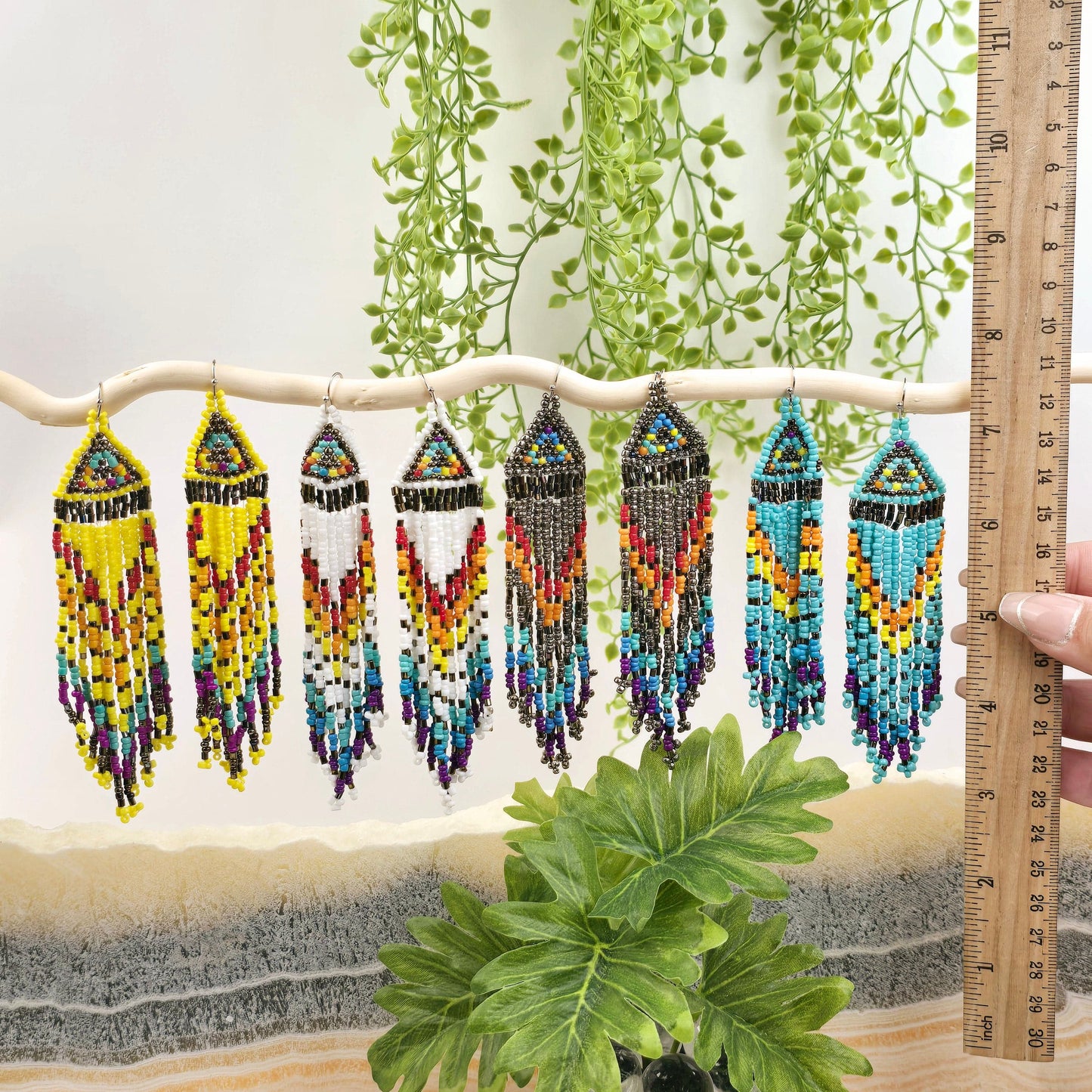Seed Bead Earrings - Small Triangle Long Fringe Pattern - You Choose Style - all four styles on white branch with ruler for size reference and plants and props in the background