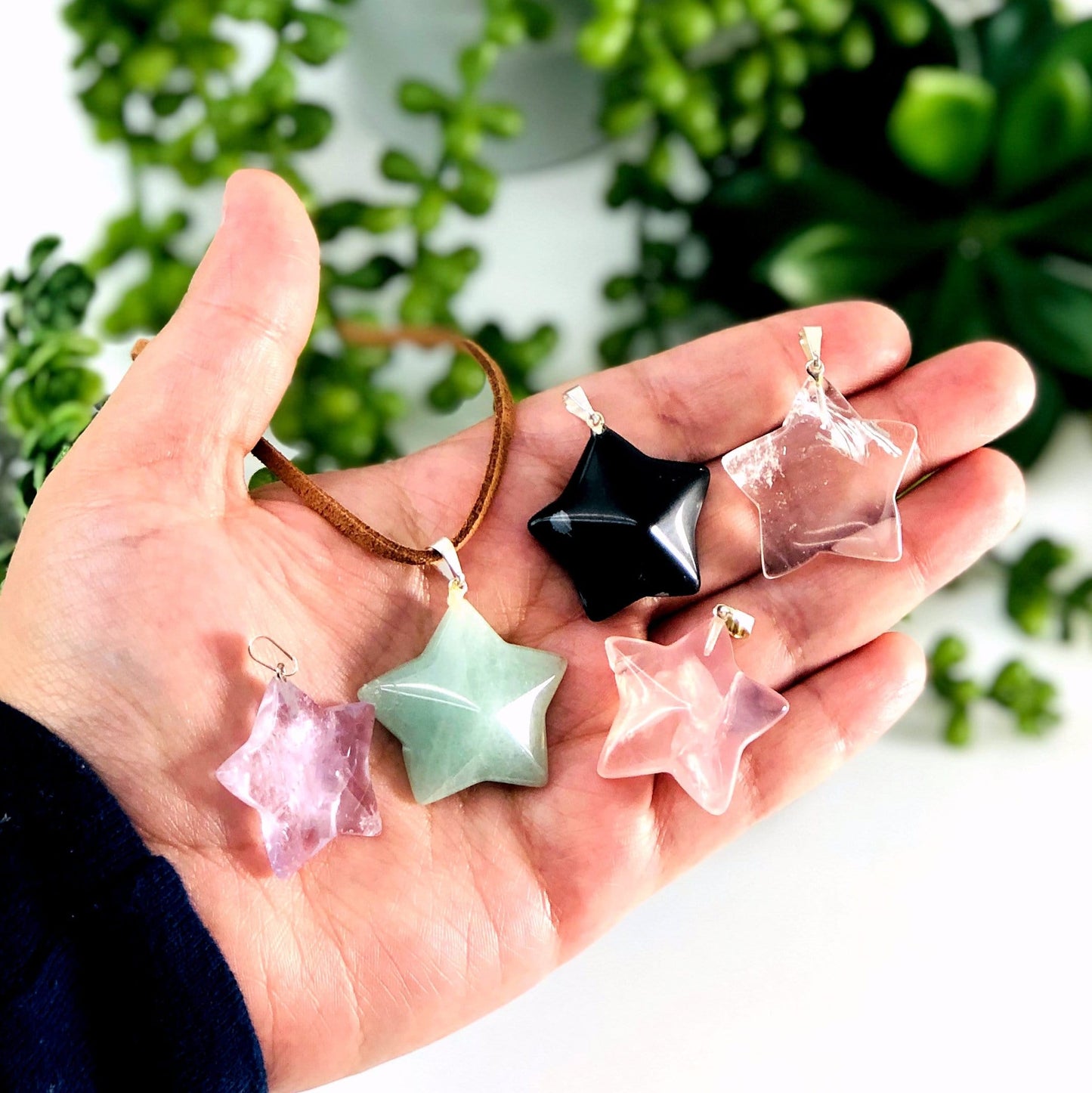 hand holding up Gemstone Star Pendants with Silver Toned Bail with decorations in the background