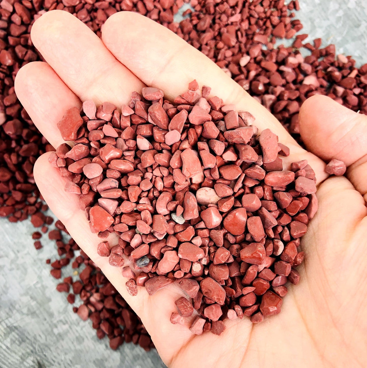 Up close shot of hand holding pile of Red Jasper Chips in front of more Red Jasper Chips