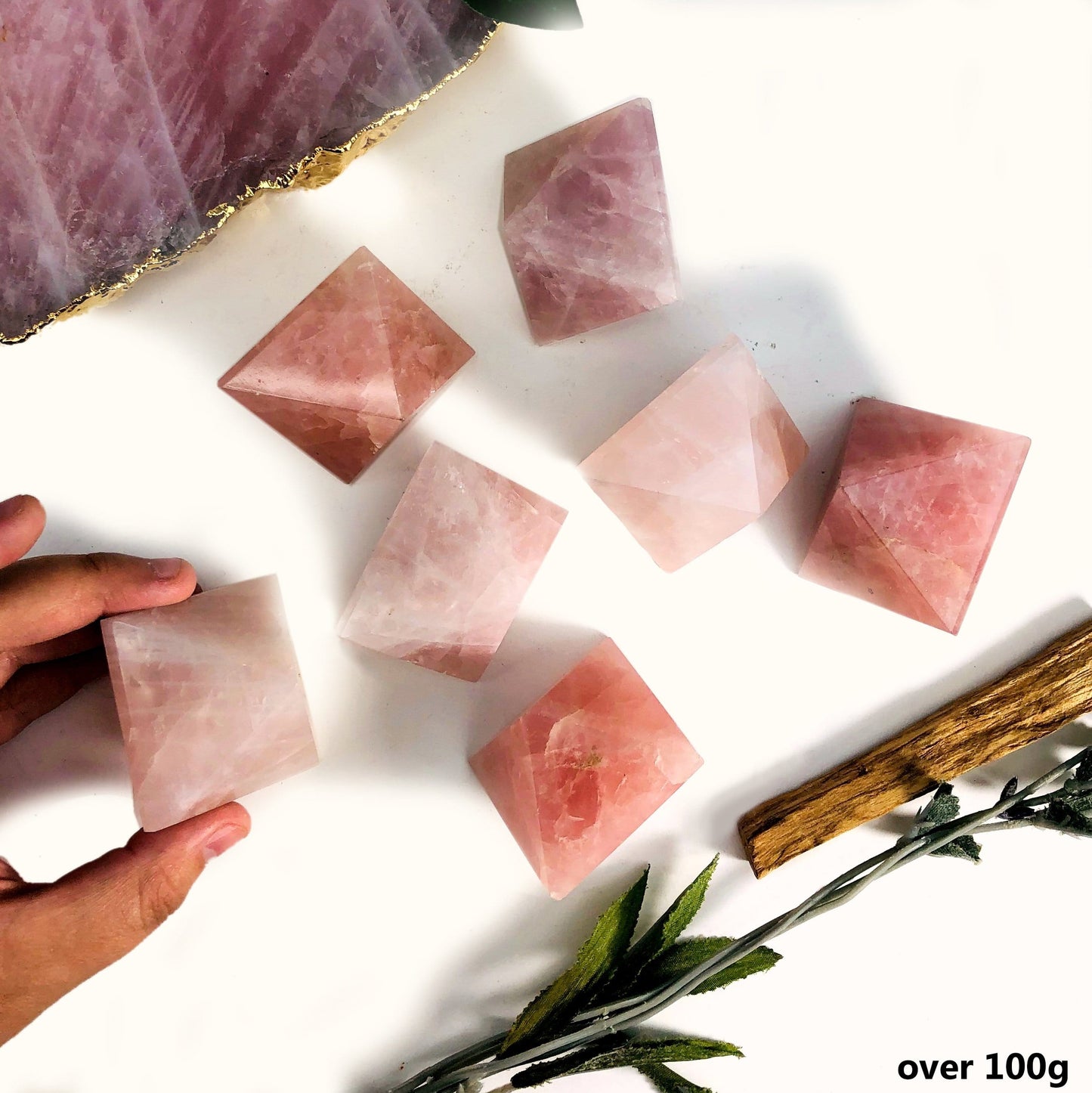 Hand holding Rose Quartz Diamond Shaped Stone over 100g with others scattered on white background with decorations