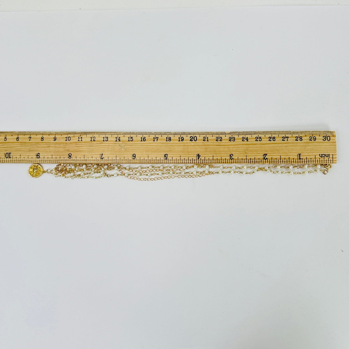 gold pearl necklace next to a ruler for size reference