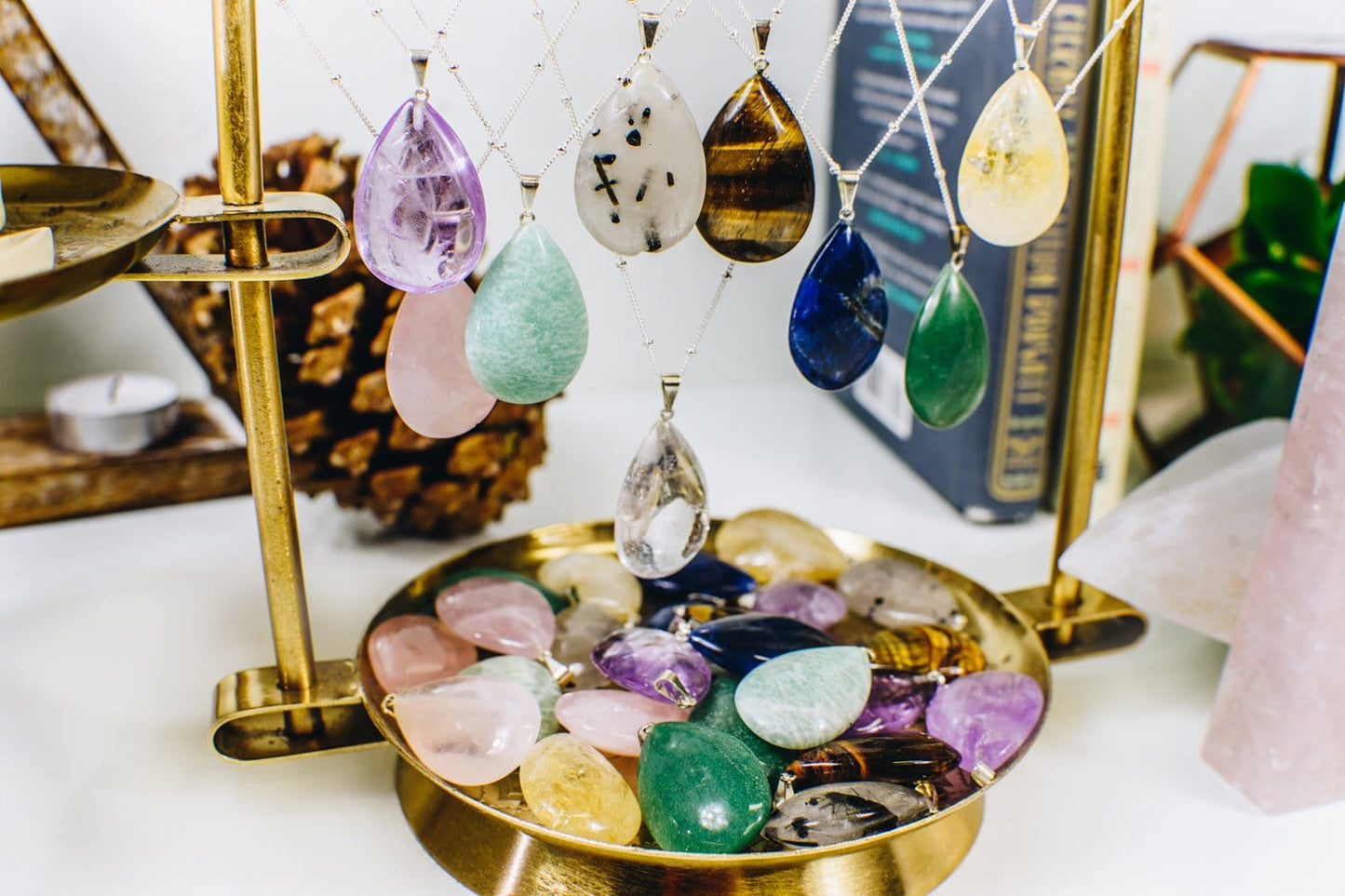 Gemstone Teardrop Pendants of various stones hanging from a holder and sitting in a tray, showing all the sshades and variations