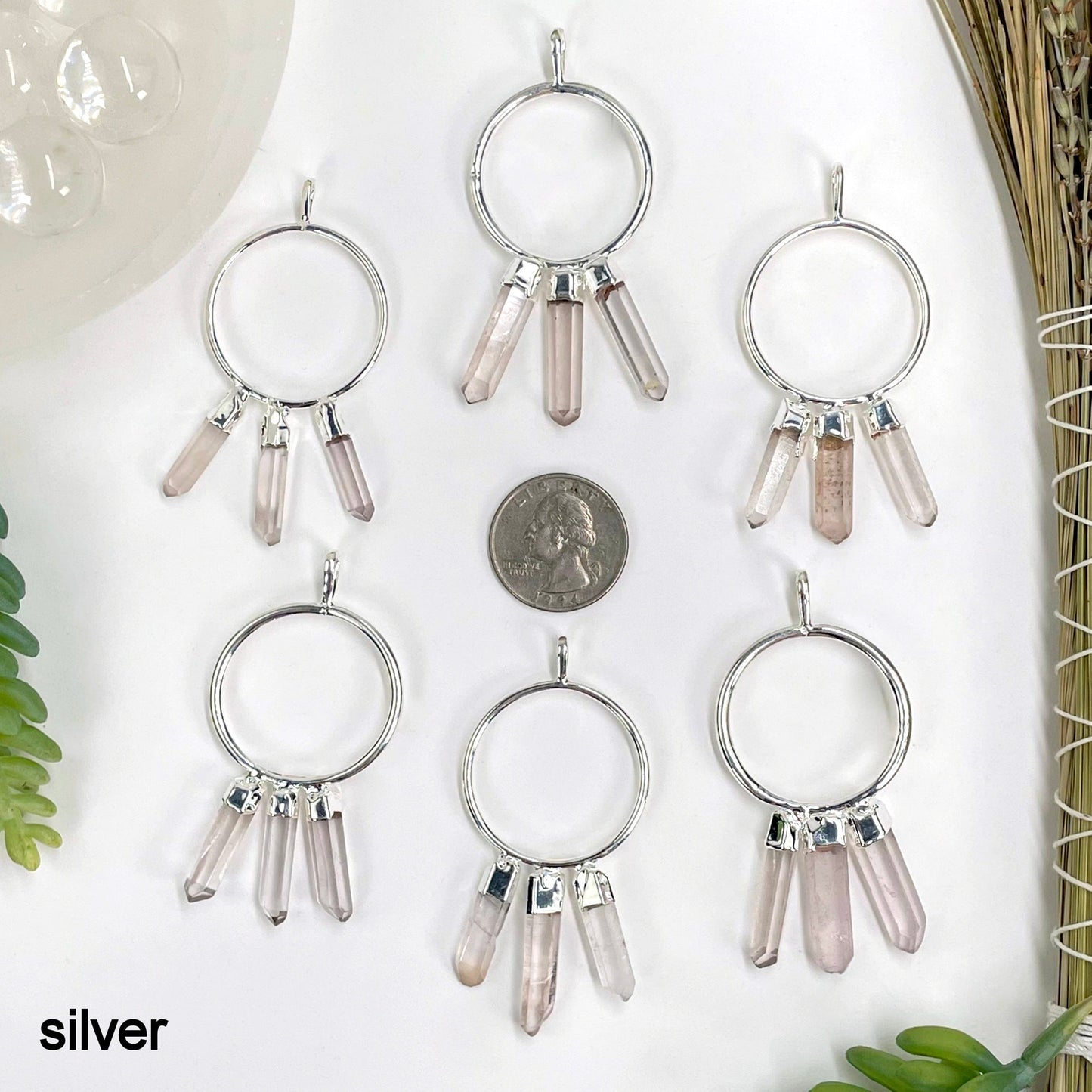 six silver triple crystal point pendants on white background with a quarter for size reference