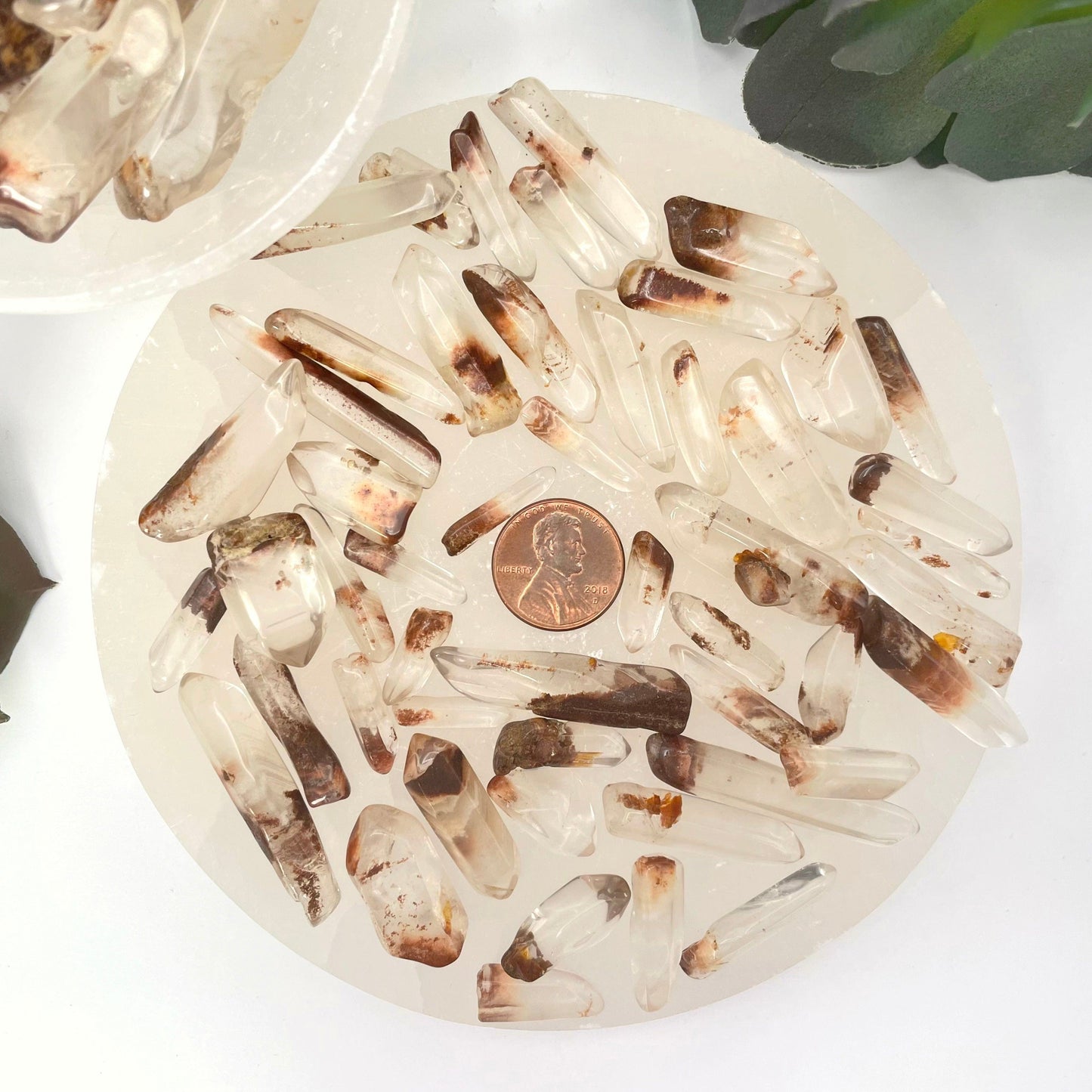 many small tumbled quartz with hematite points on display with penny for size reference