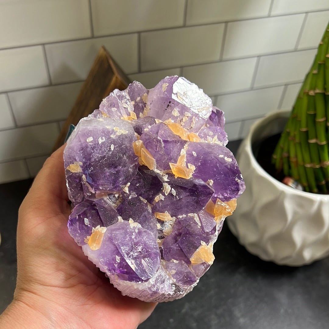Amethyst cluster with orange calcite speckled throughout held in a woman's hand