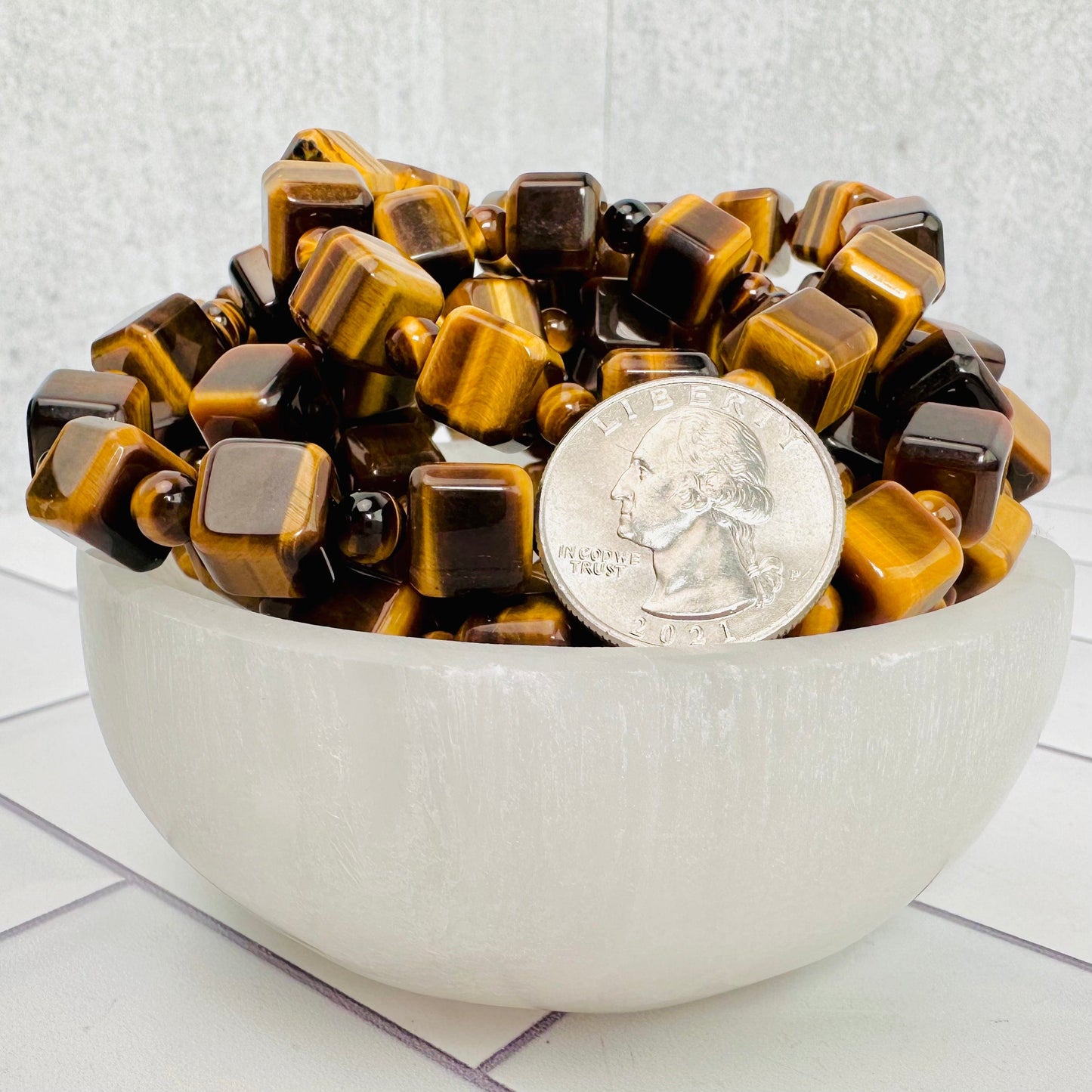 Various Tigers eye bracelets displayed in small selenite bowl with a quarter next to them for size reference.