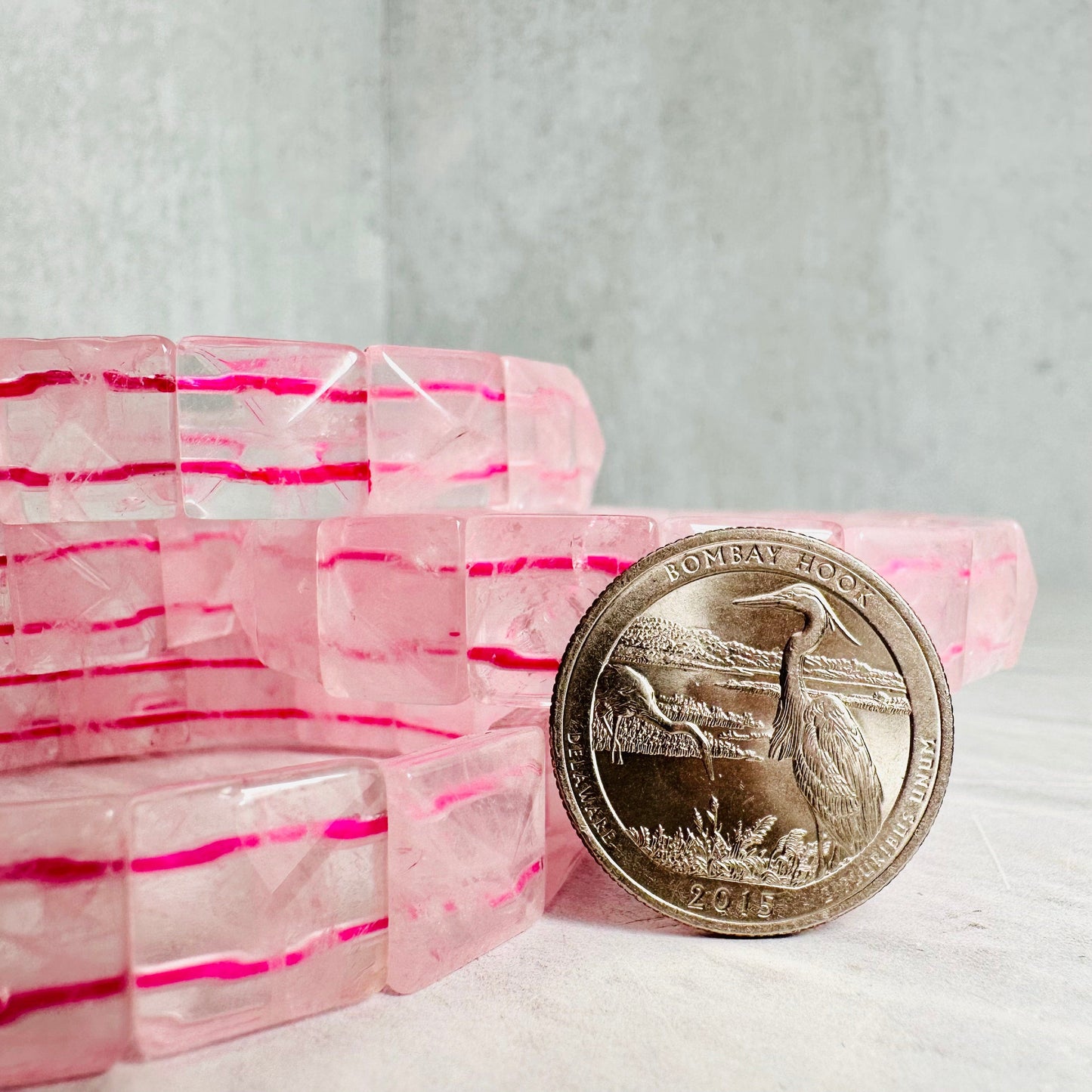 Stacked Rose Quartz Square Bead Bracelets next to a quarter for size reference.