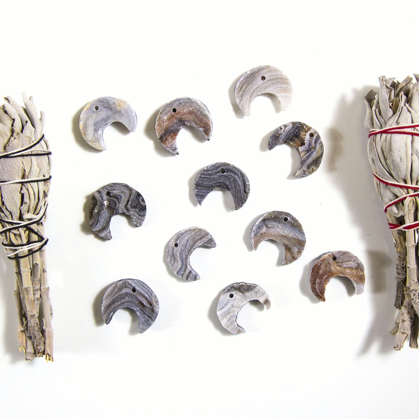 11 Raw Chalcedony Moon Crescents with sage on a white background