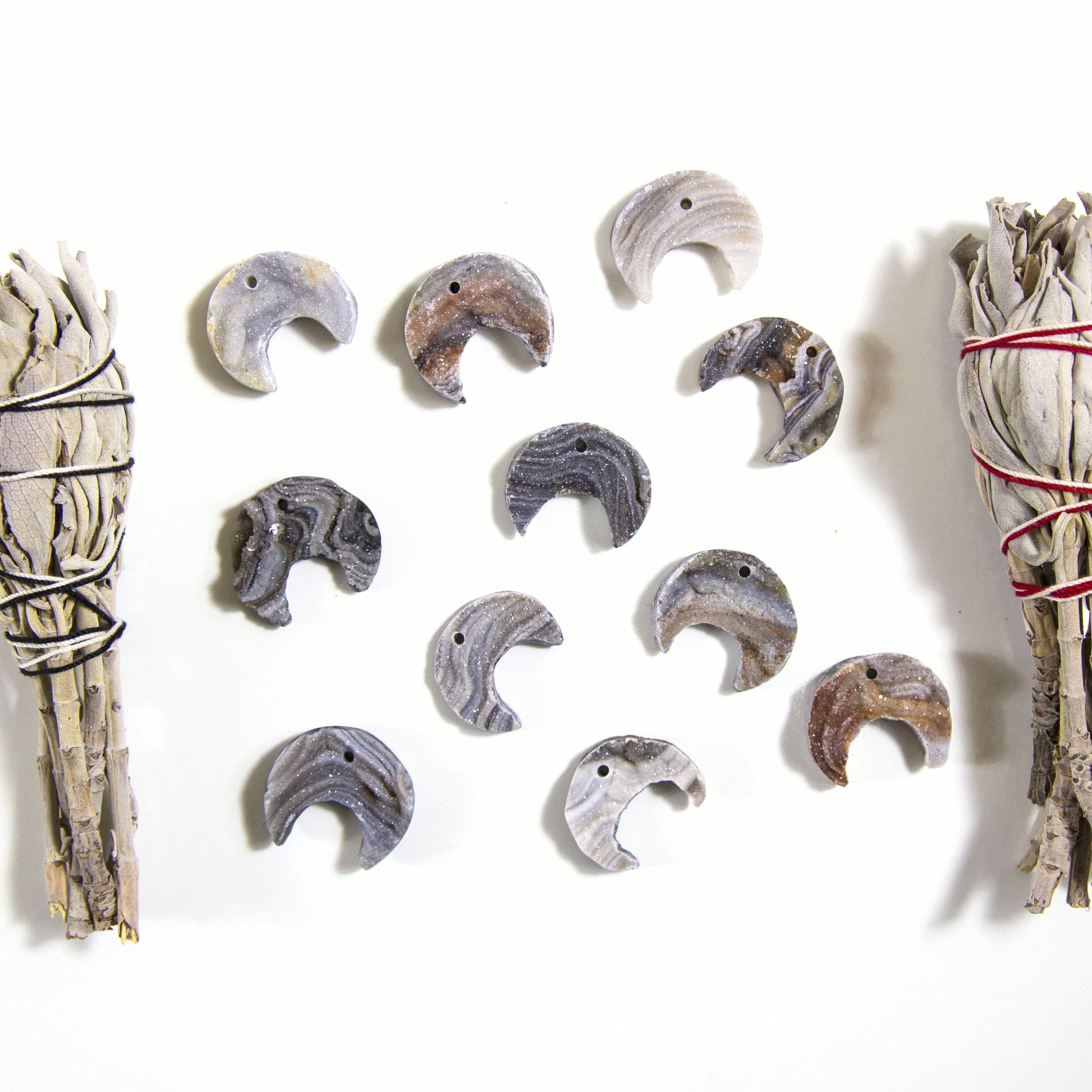 11 Raw Chalcedony Moon Crescents with sage on a white background