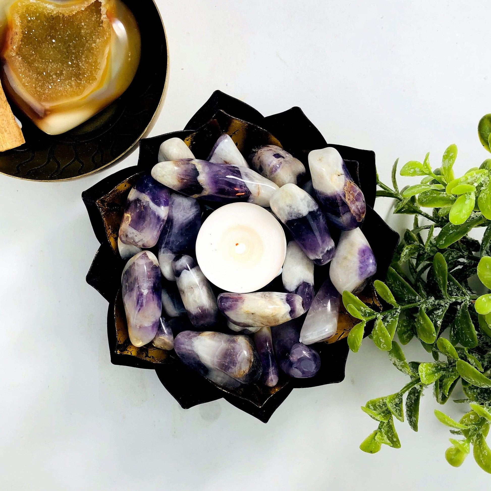 A gold bowl holding Chevron Amethyst Tumbled Gemstones and a votive