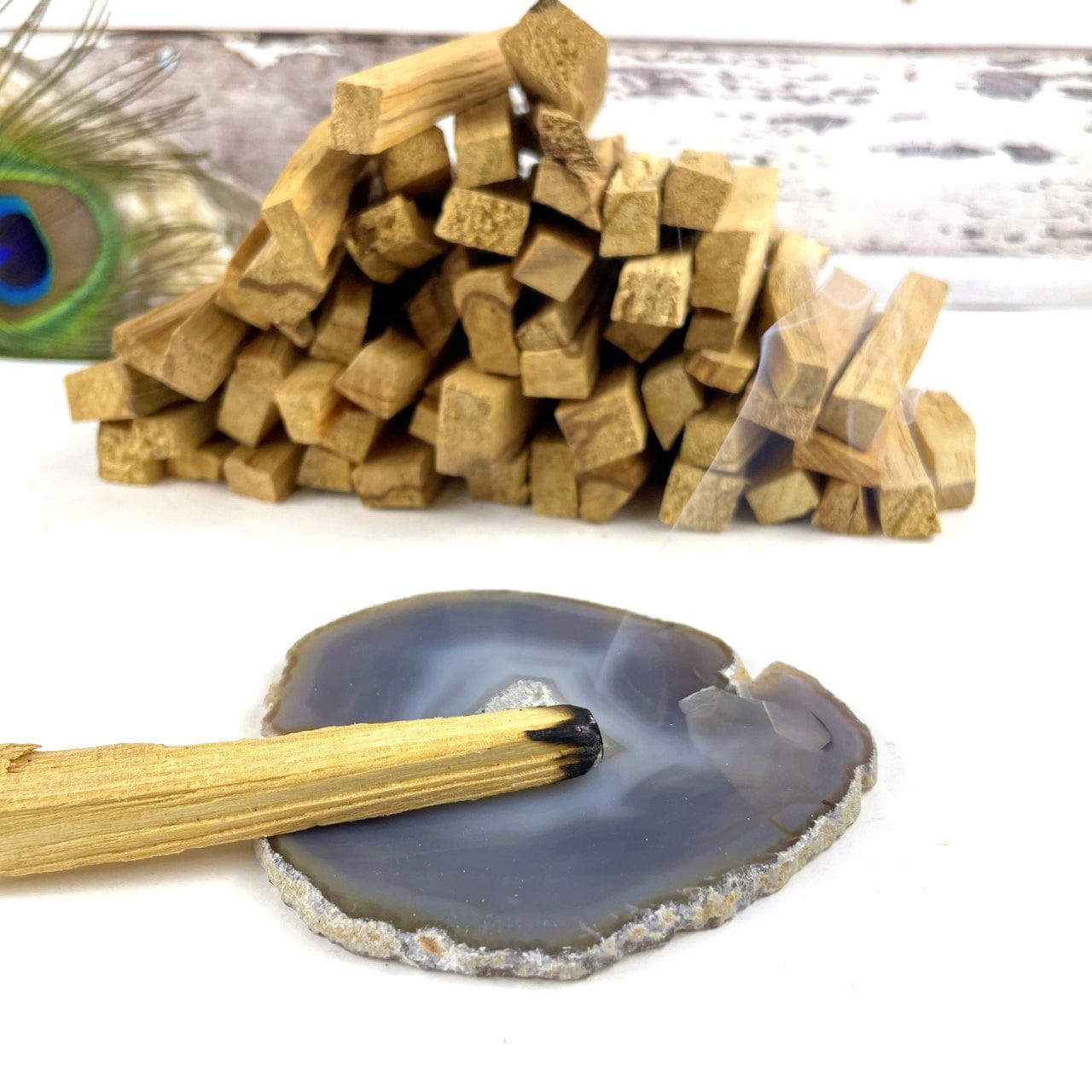 A pile of palo santo sticks on a white background.  One is lit and the tip is placed on a gray agate slice.