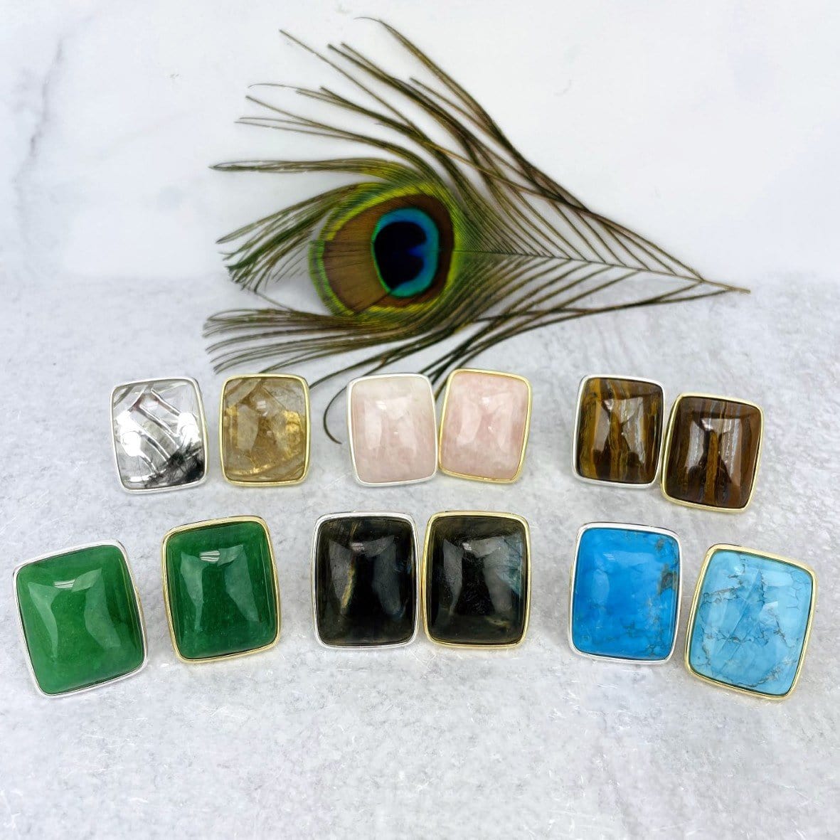 various stone rings in gold and silver displayed in front of peacock feather