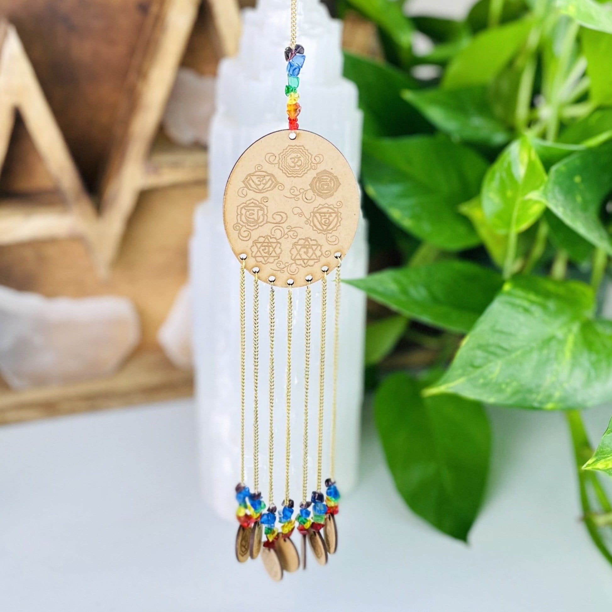 Engraved Wooden 7 Chakras hanged next to green leaves. 