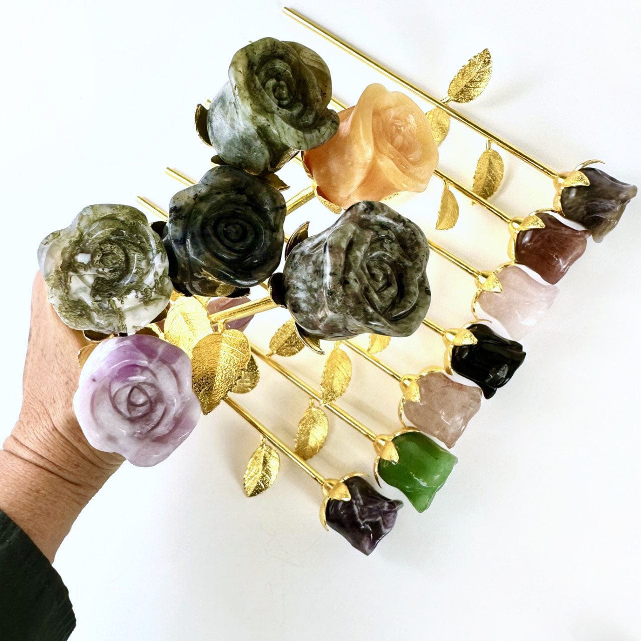 carved stone roses layed out on a table with others in a hand for size reference