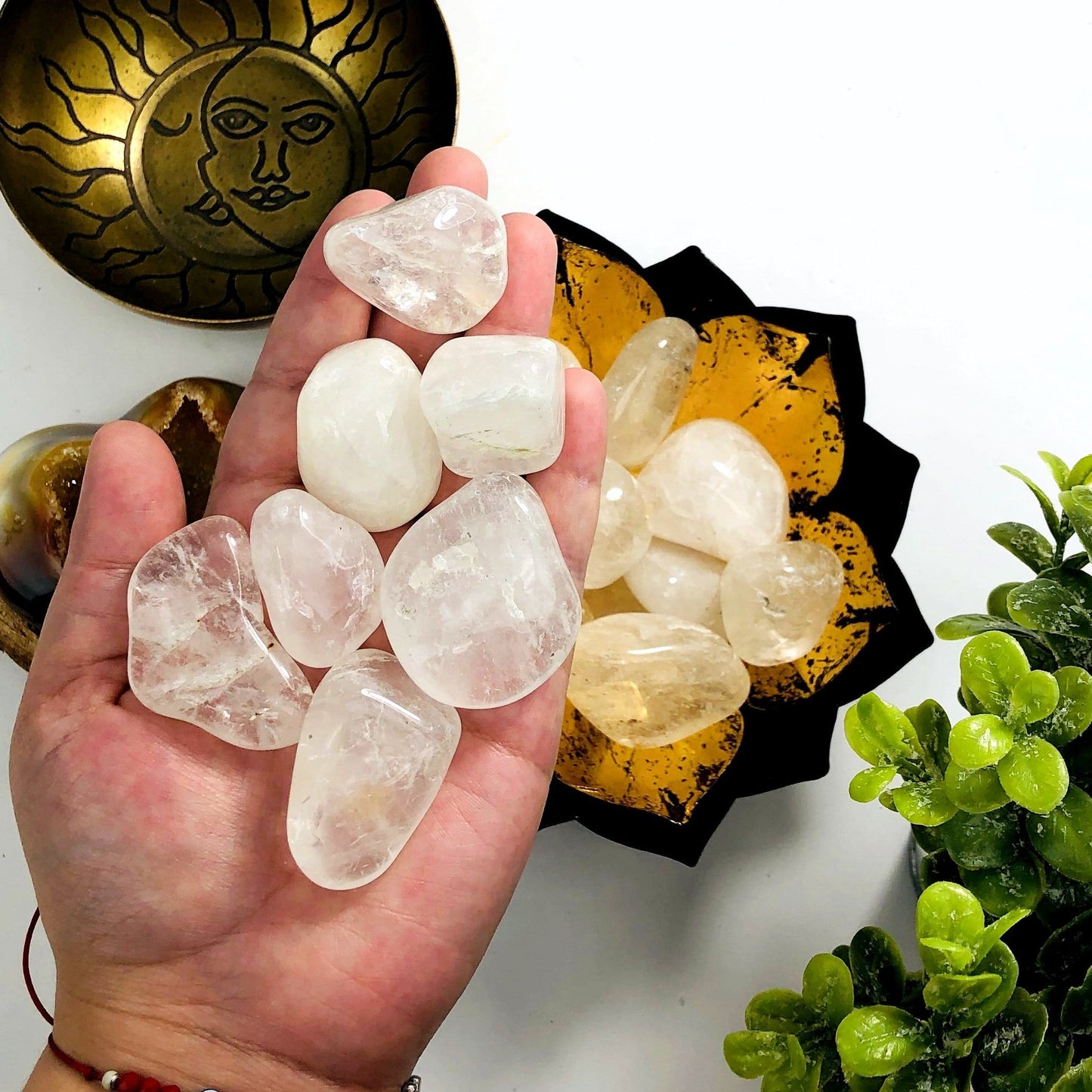 Crystal Quartz tumbled stones in a hand with more in a lotus metal bowl behind it.  8 pieces fit in the hand.