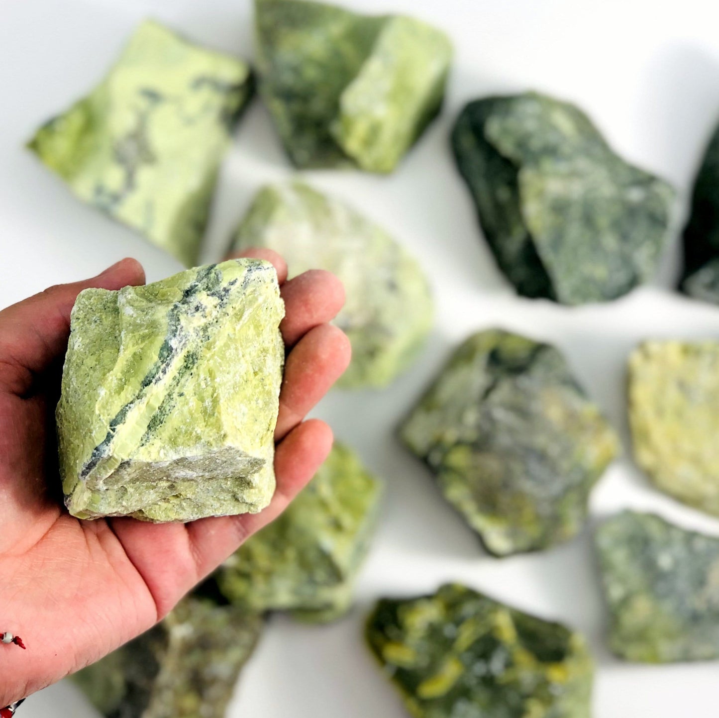 one serpentine rough stone in hand for size reference with others in background