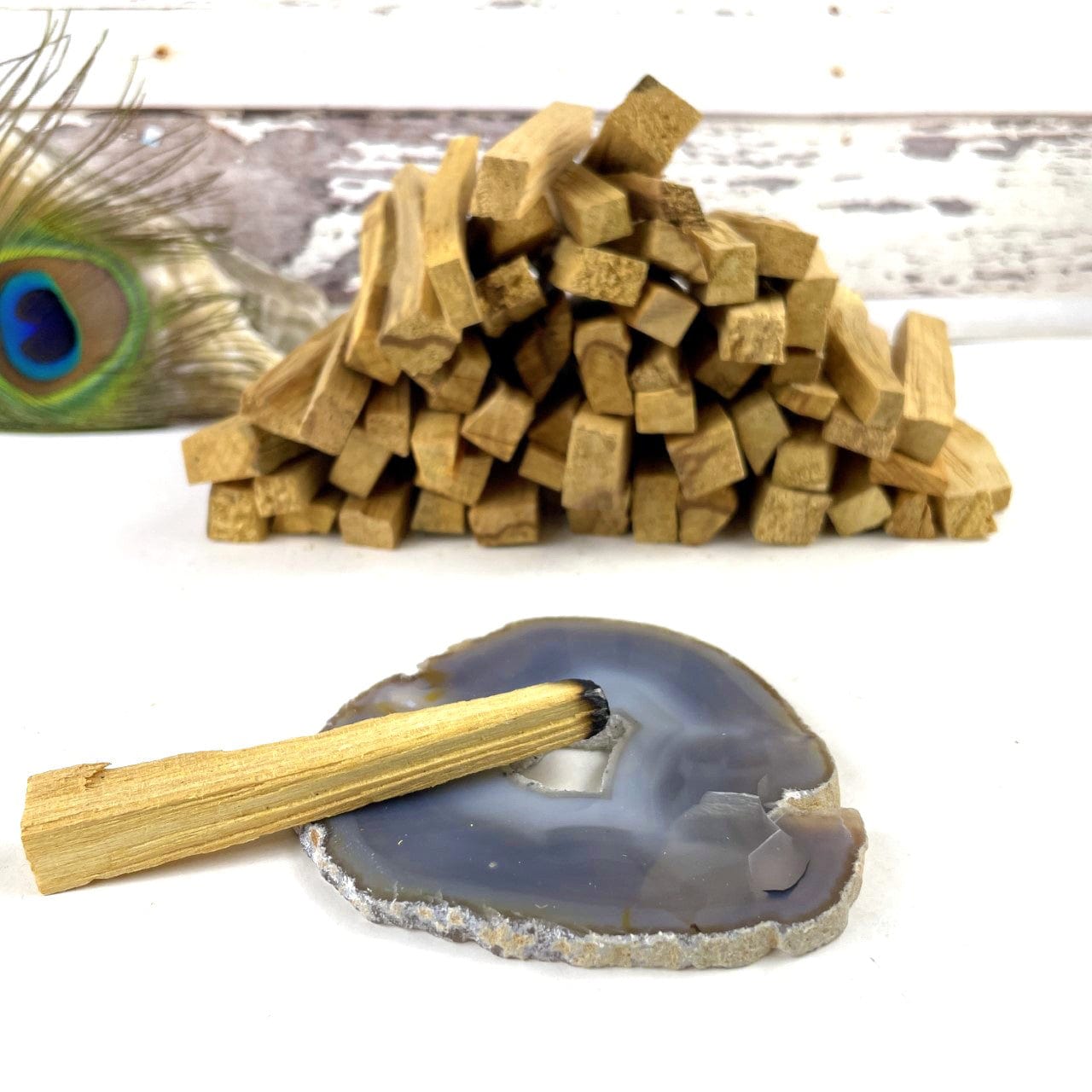 A pile of palo santo sticks on a white background.  One is lit and the tip is placed on a gray agate slice.