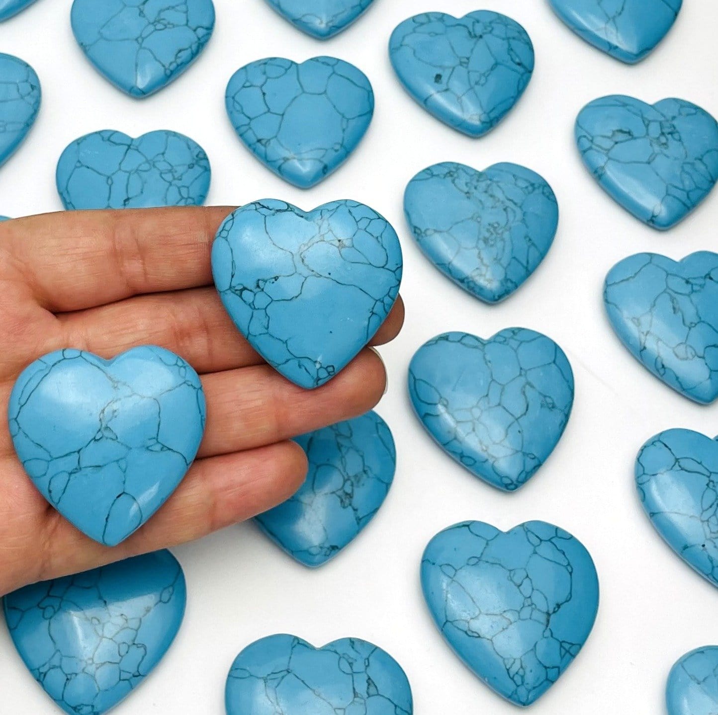 hand holding up 2 turquoise howlite hearts with others in the background
