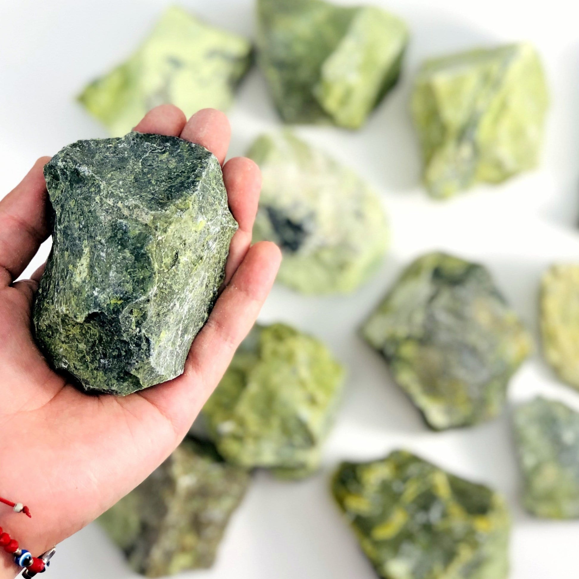 one serpentine rough stone in hand for size reference with others in background