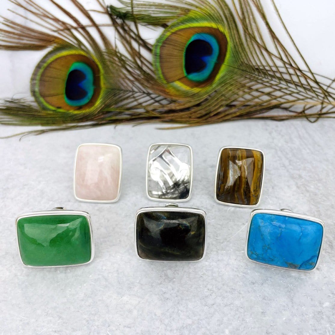 front view of silver stone rings in front of peacock feather