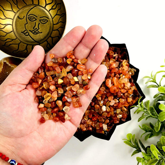 Small orange carnelian chips held in a hand with more in a bowl in the background,