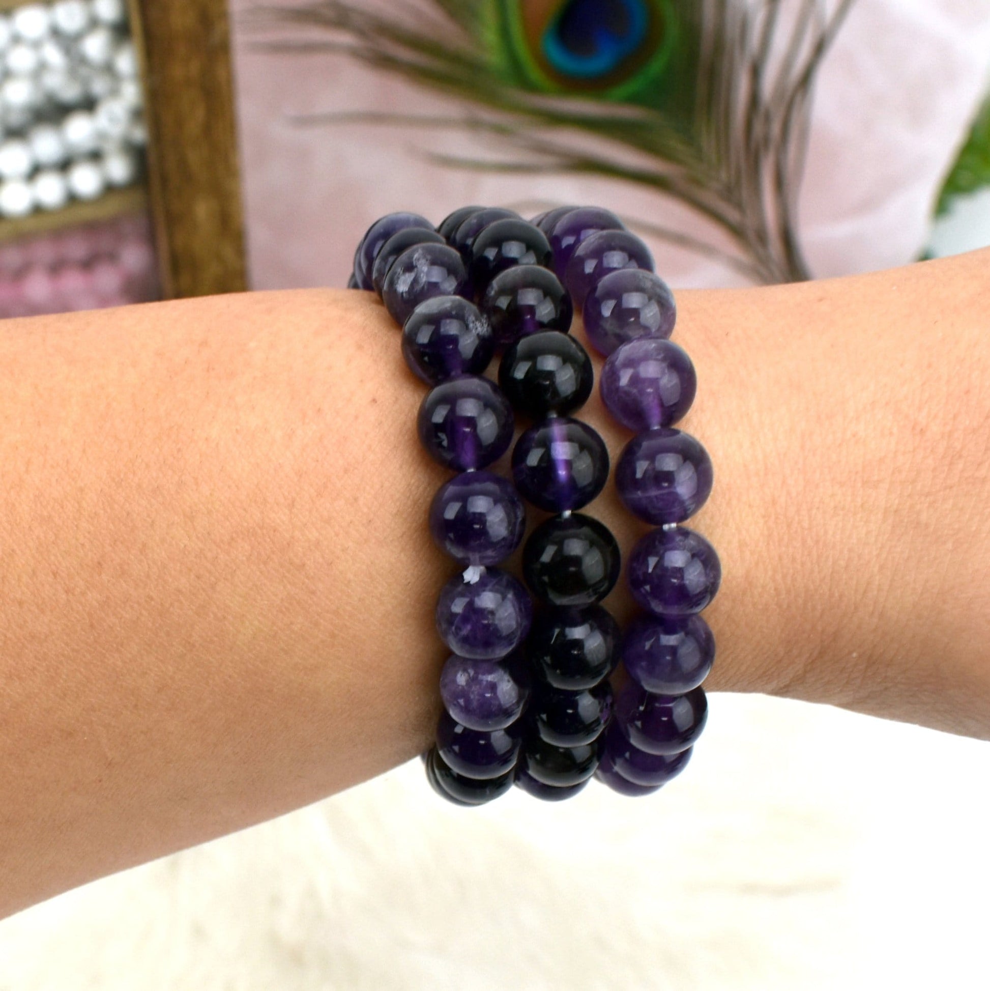 write wearing 3 Amethyst Round Bead Bracelets with decorations in the background