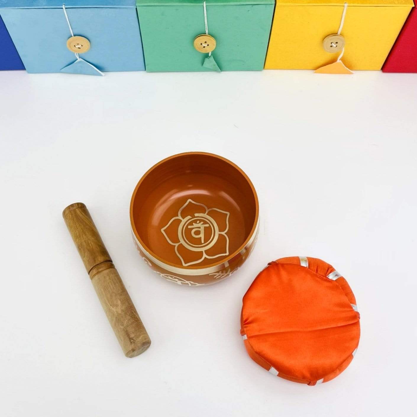 Brass Tibetan Chakra Singing Bowl next to a pillow, and a mallot with the boxes that the bowls come in behind