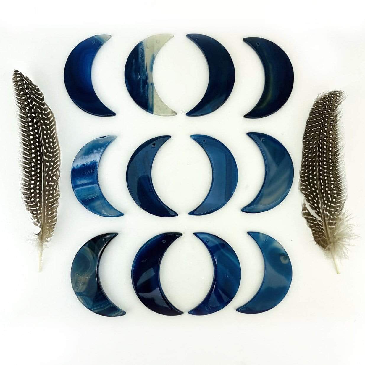 Twelve agate moons displayed on a white surface next to feathers.