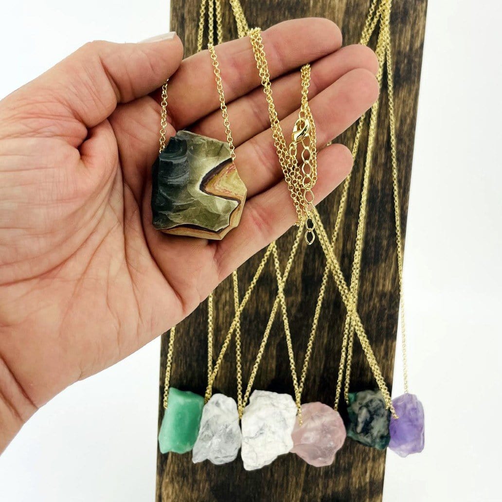 Hand holding 1 Healing Stone Necklace with others in the background