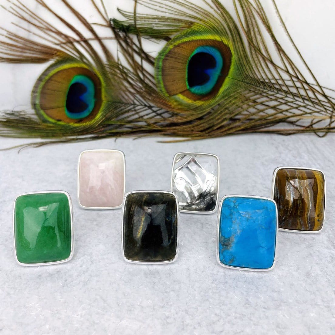 front view of silver stone rings in front of peacock feather