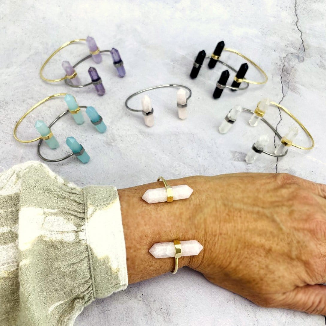 wrist wearing rose quartz Crystal Point Cuff in gold with others in the background