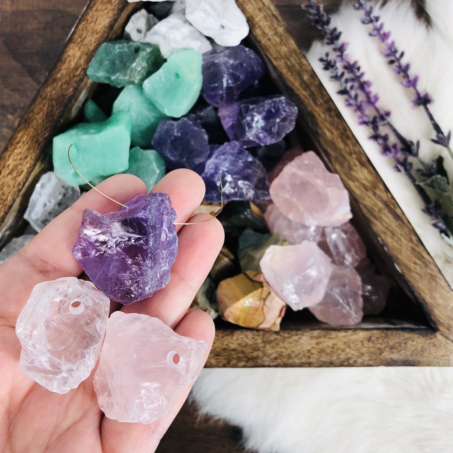3 Rough Stone Beads in hand with a wire going through one of them. Triangular box filled with more blurred in the background