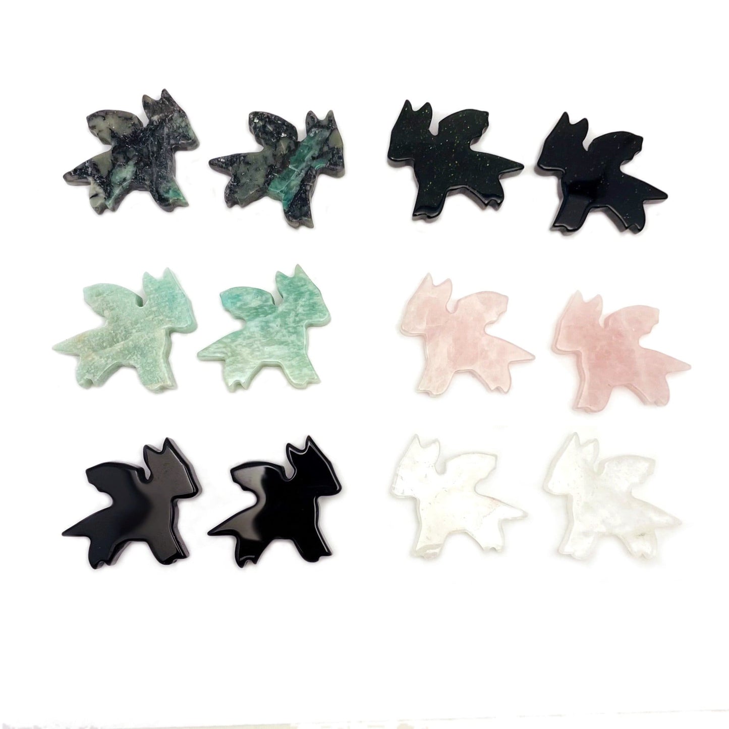 Gemstone Dragon Cabochons laid out in twos to show color pattern shape variations and gemstone options such as emerald amazonite black onyx green goldstone rose quartz crystal quartz on white background