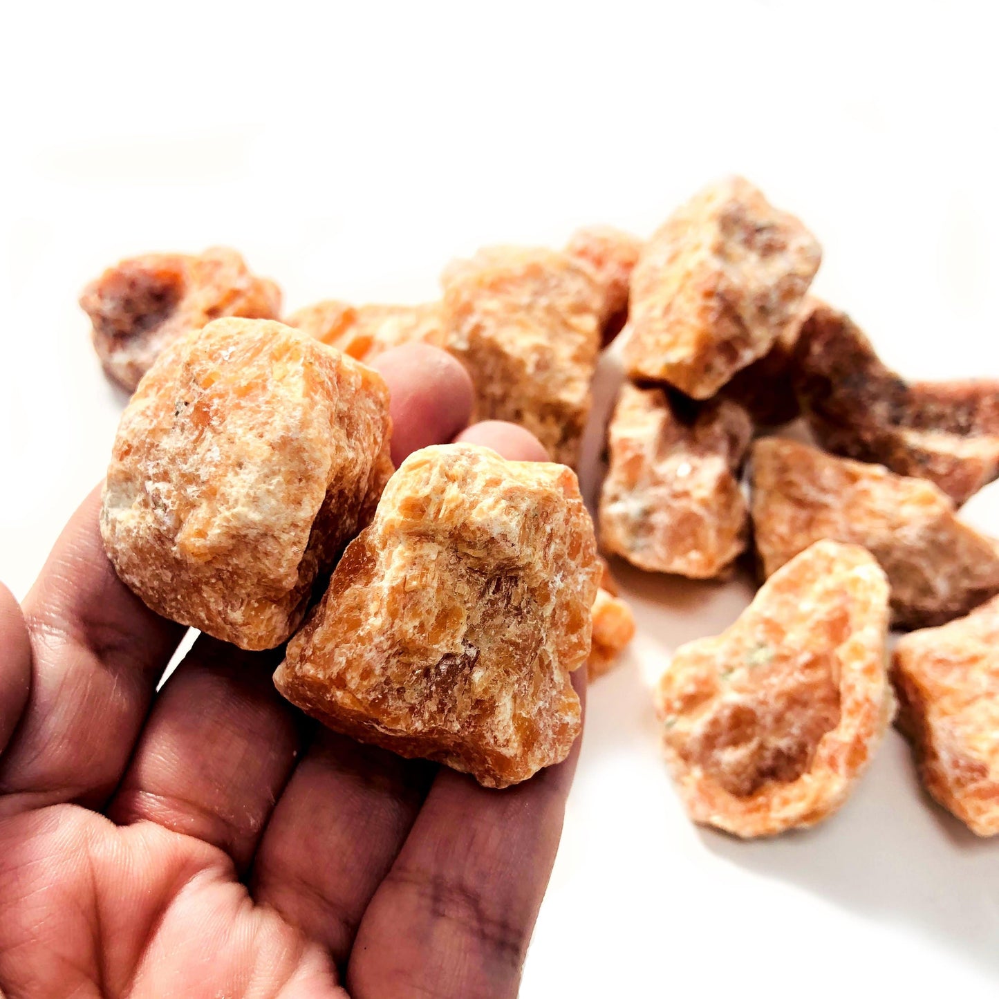 hand holding up 2 orchid calcite raw stones with others blurred on white background