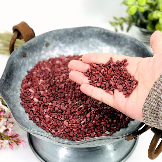 Hand holding up pile of Red Jasper Chips in front of bowl filled with Red Jasper Chips