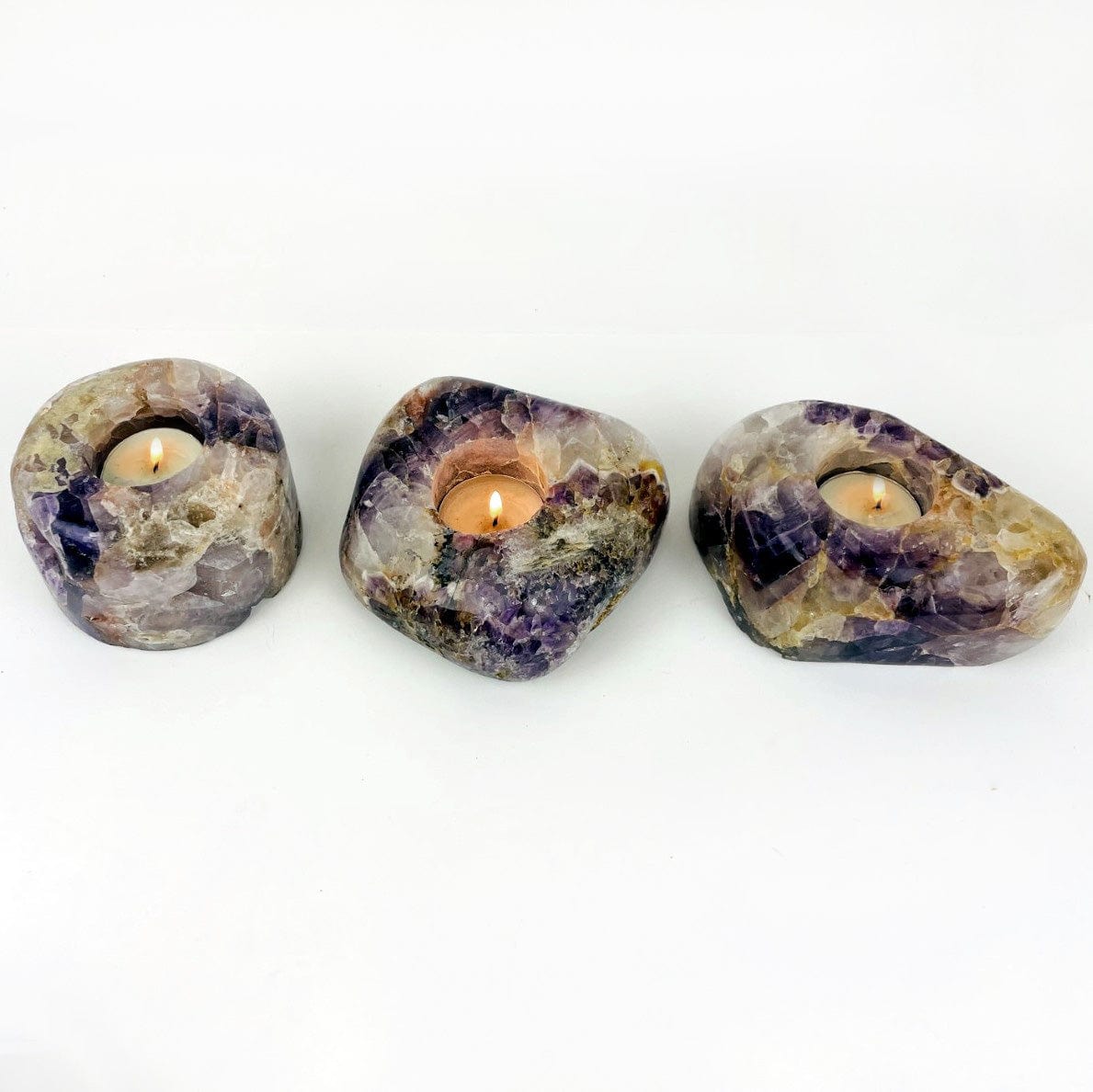 3 freeform shapes of chevron amethyst  with a lit candle in them