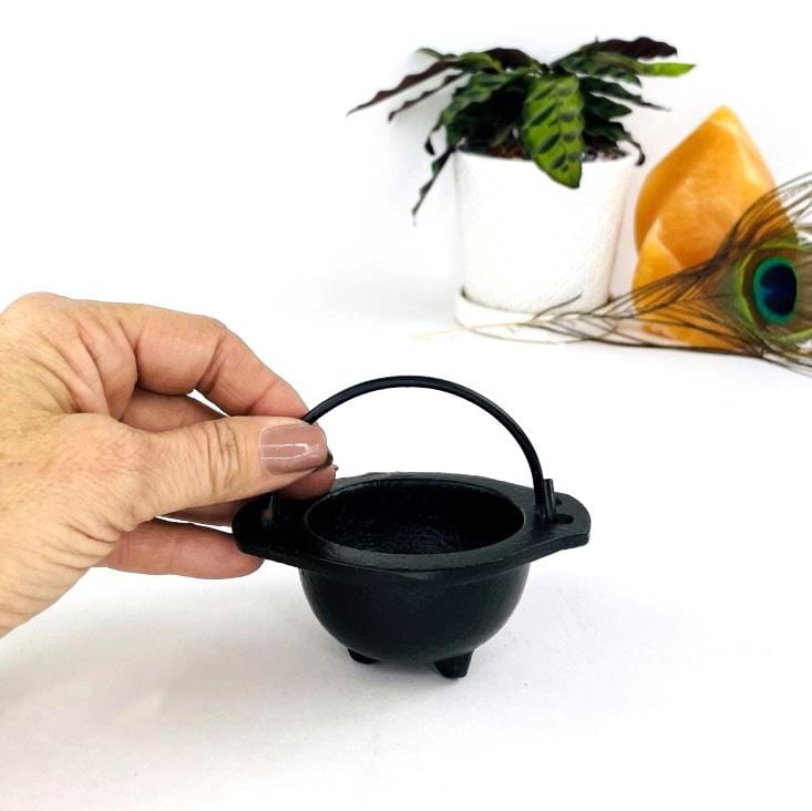 Little iron black couldron next to a woman's hand on a white background.