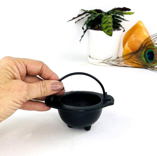 Little iron black couldron next to a woman's hand on a white background.