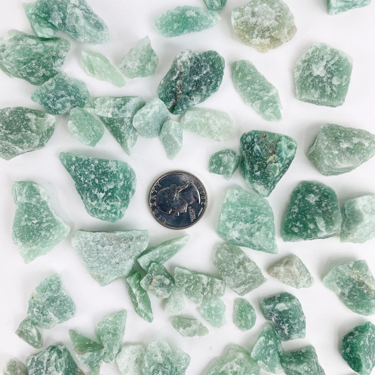 Green Quartz Stones spread out on a table with a quarter for size