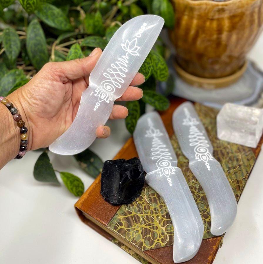 selenite knife with unalome engraving in hand for size reference with others in background