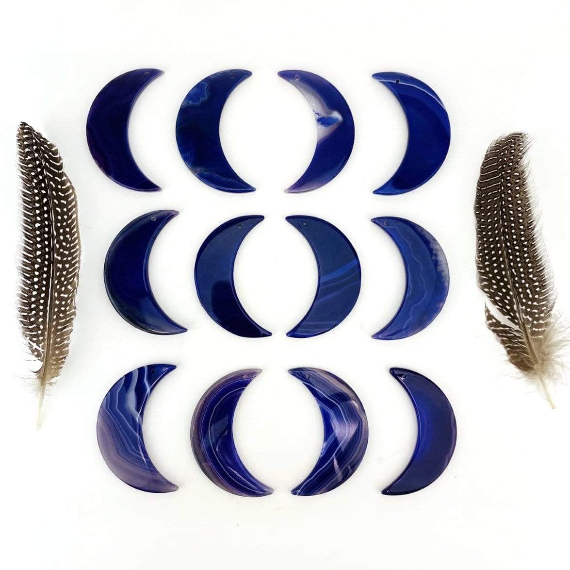 Twelve purple agate moons displayed on a white surface next to feathers.