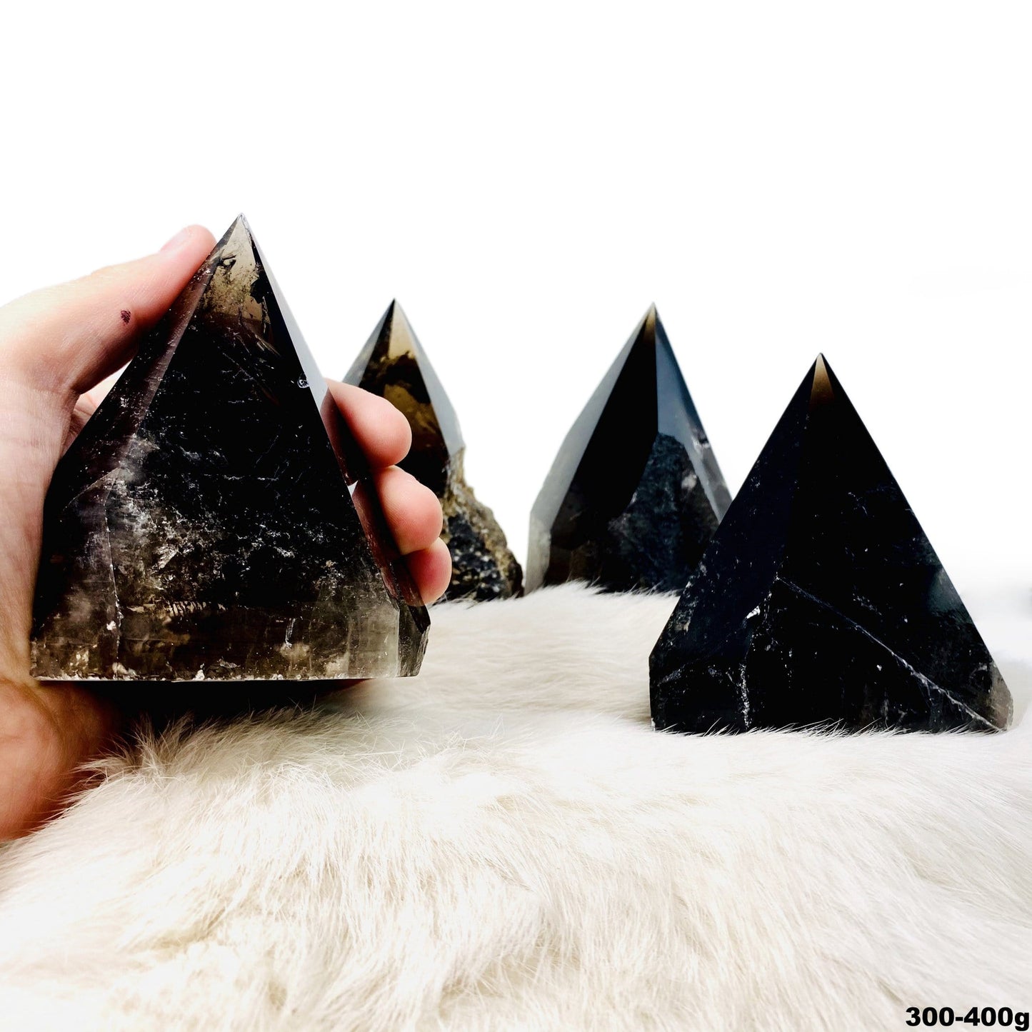 four 300g - 400g smokey quartz semi polished points on display for possible variations with one in hand for size reference