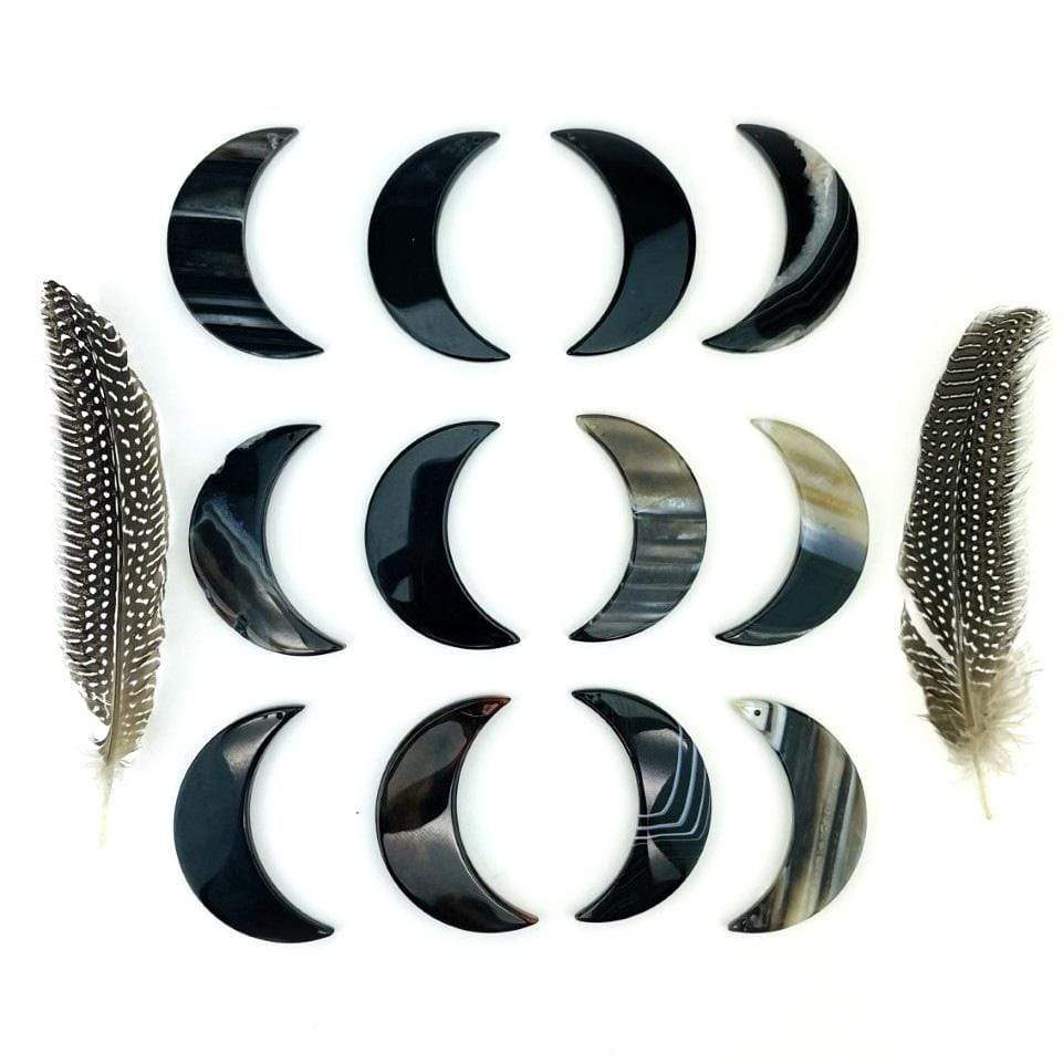 Twelve black agate moons displayed on a white surface next to feathers.