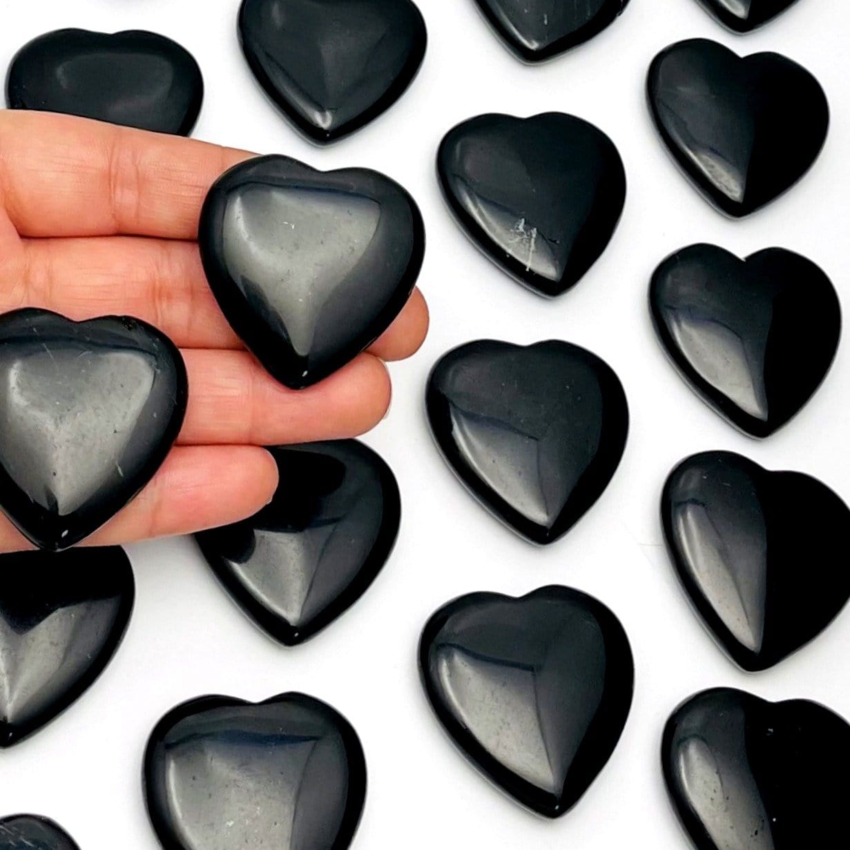 hand holding up 2 Black Obsidian Hearts with others in the background