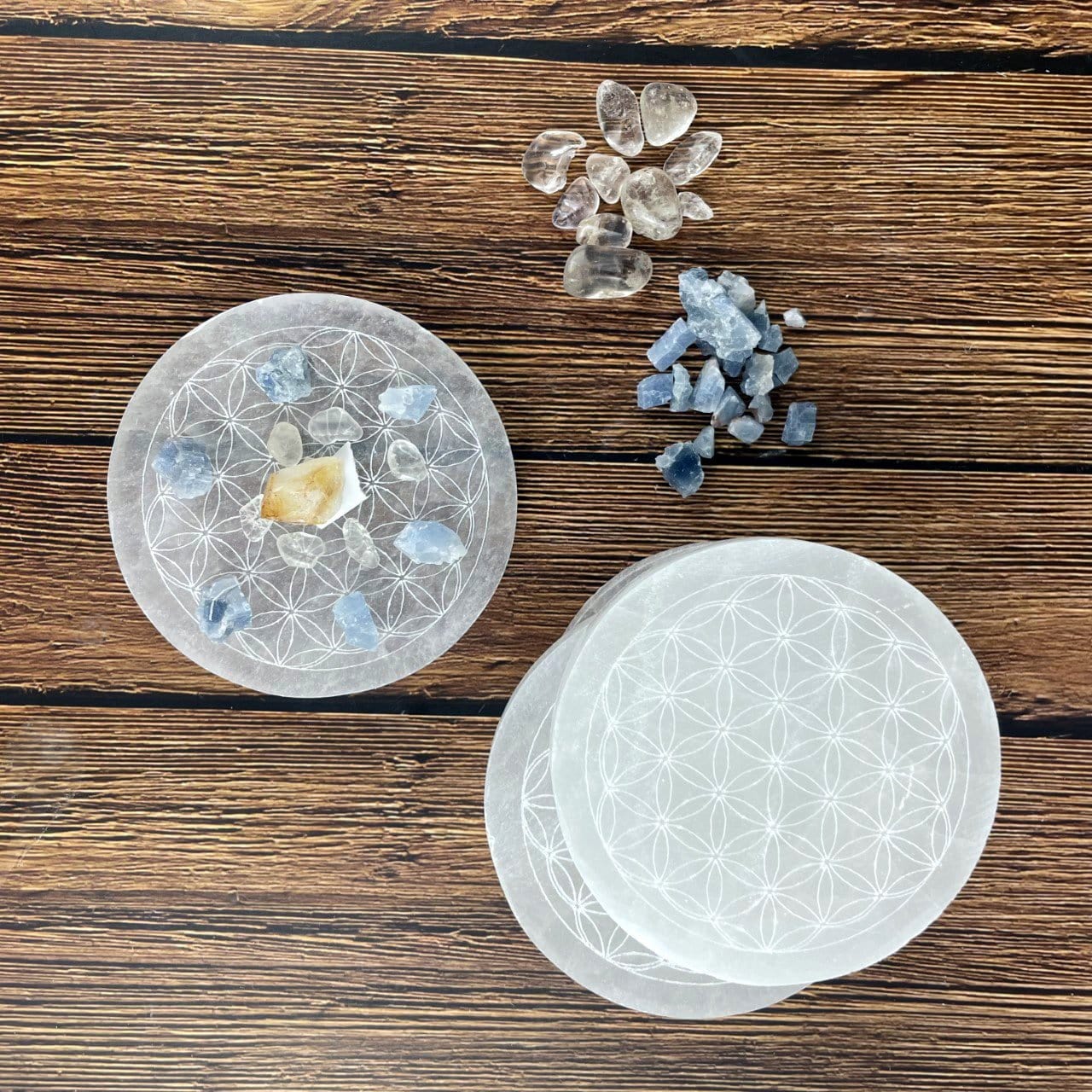 overhead view of selenite round plate engraved with flower of life with charging stones on engraving with others on display