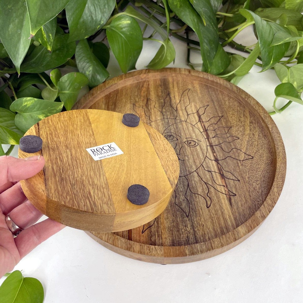 backside of small mango wood sun and moon tray showing 3 felt round pads on the bottom and a rock paradise sticker that says made in india.  Large tray is in the photo showing the front side