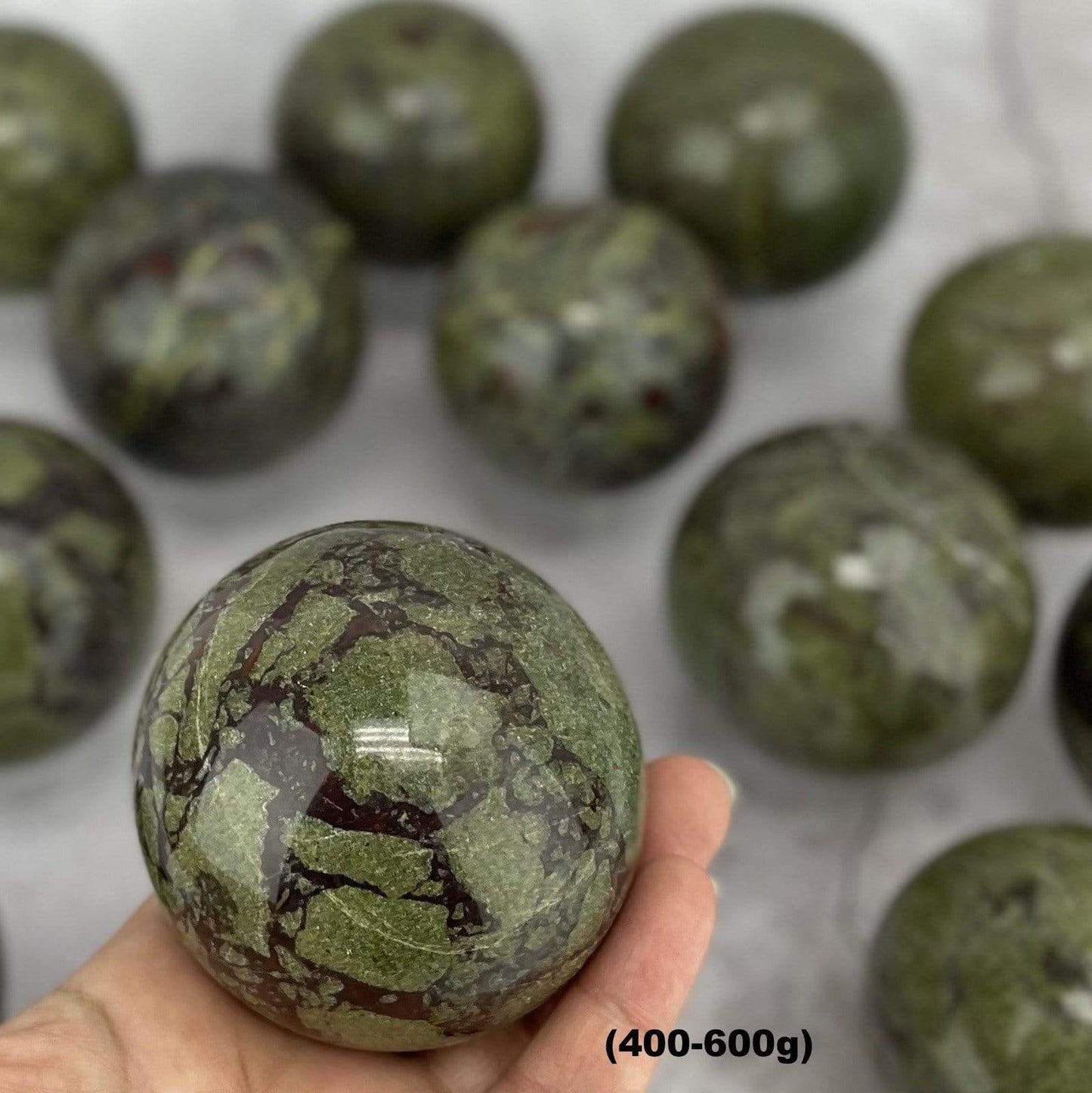 Dragon Blood Stone Sphere in Hand on Gray Background.