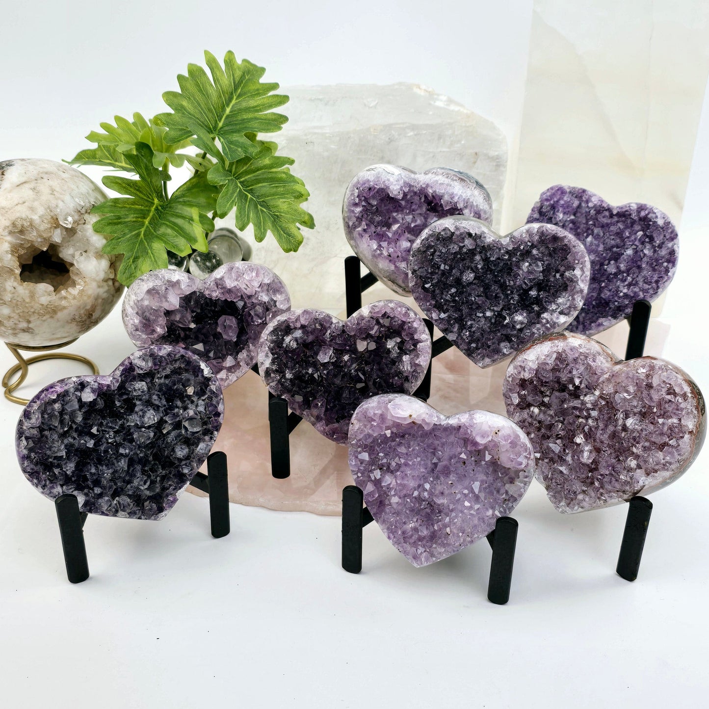 Amethyst Crystal Heart on Metal Tripod Stand front view on stone platter on bright background with props and plants