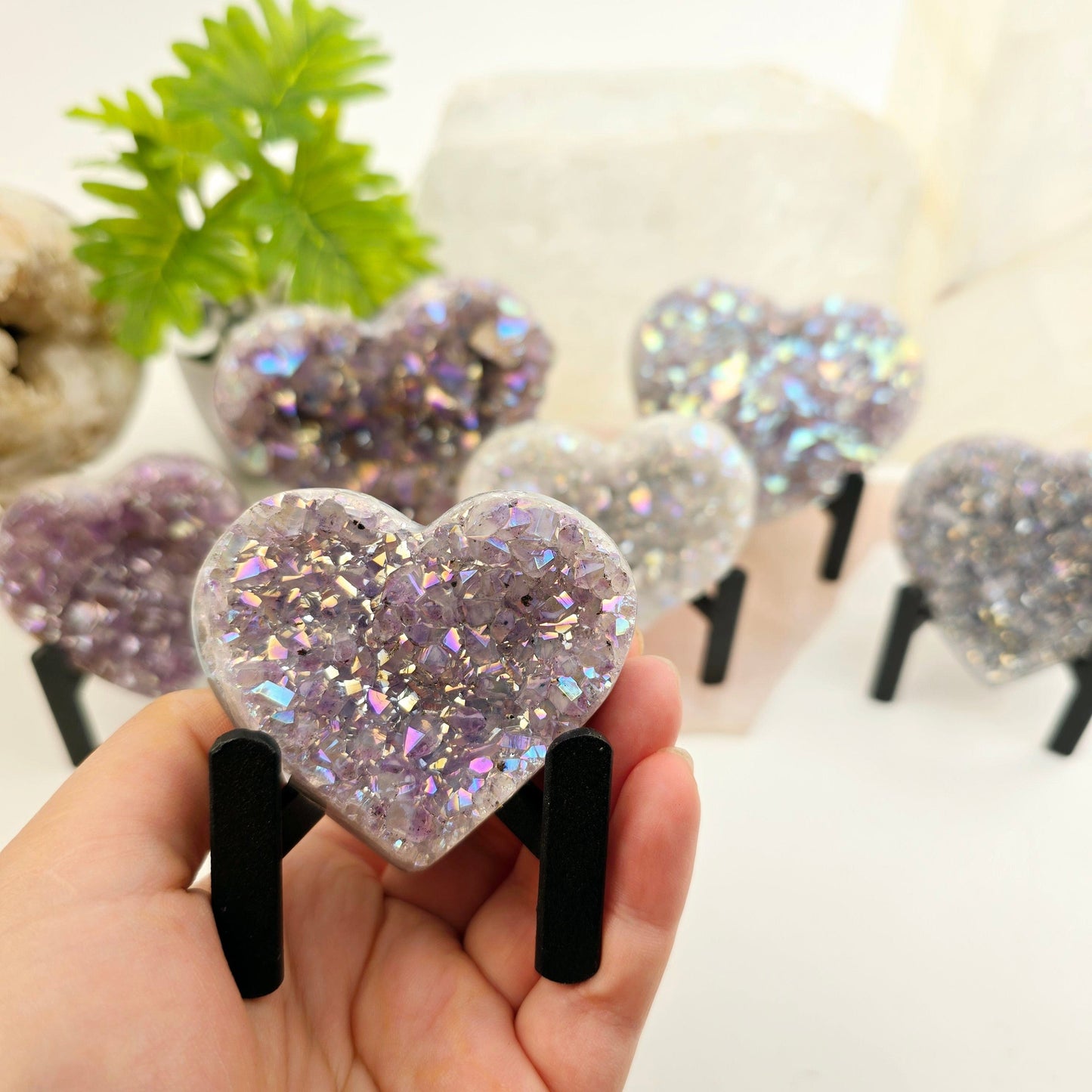 Angel Aura Amethyst Crystal Heart on Metal Tripod Stand - one in hand for size reference with others in the background with plants and props