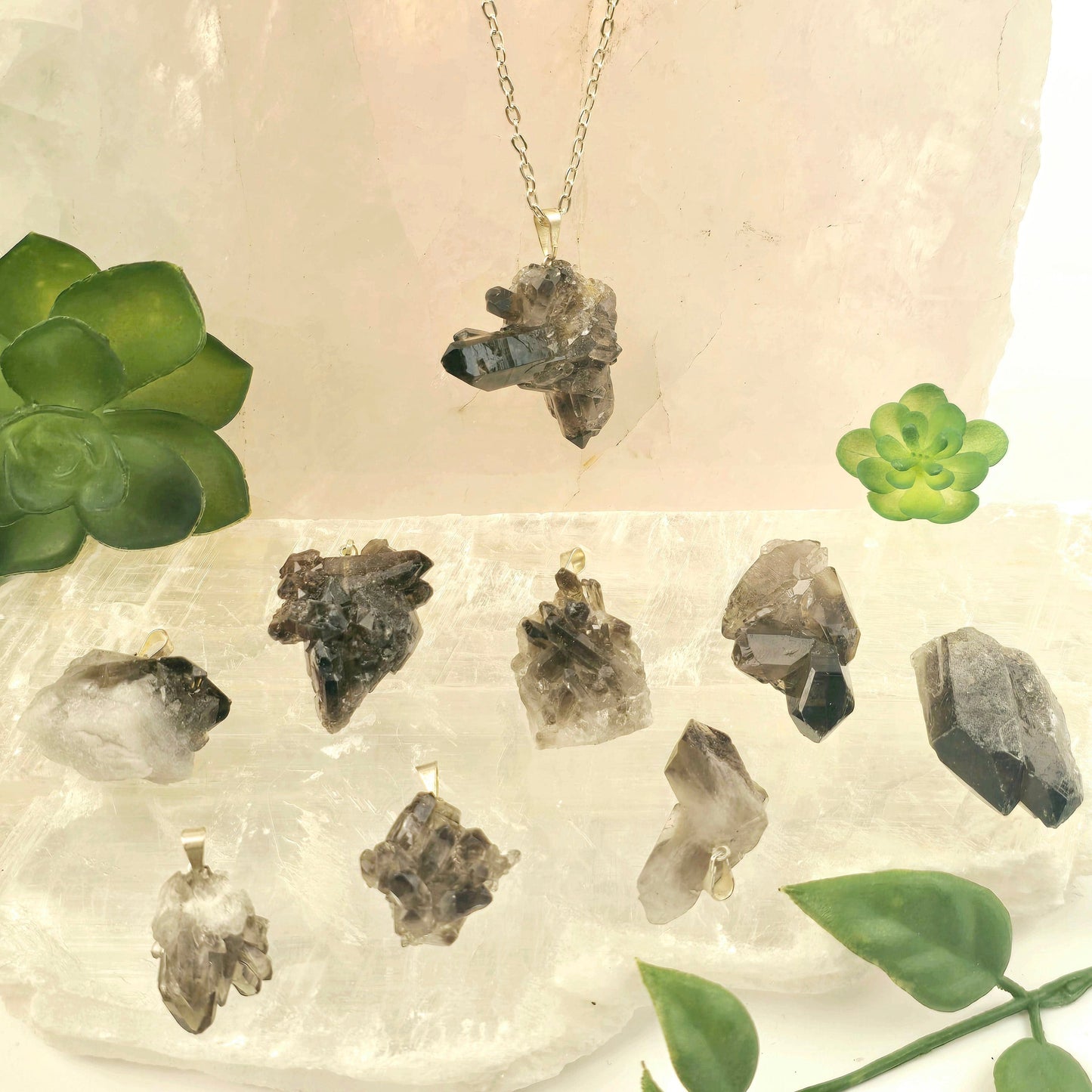 Smokey Quartz Rough Crystal Cluster Pendant with Silver Bail - one on chain with others on selenite platter with props and plants in the background